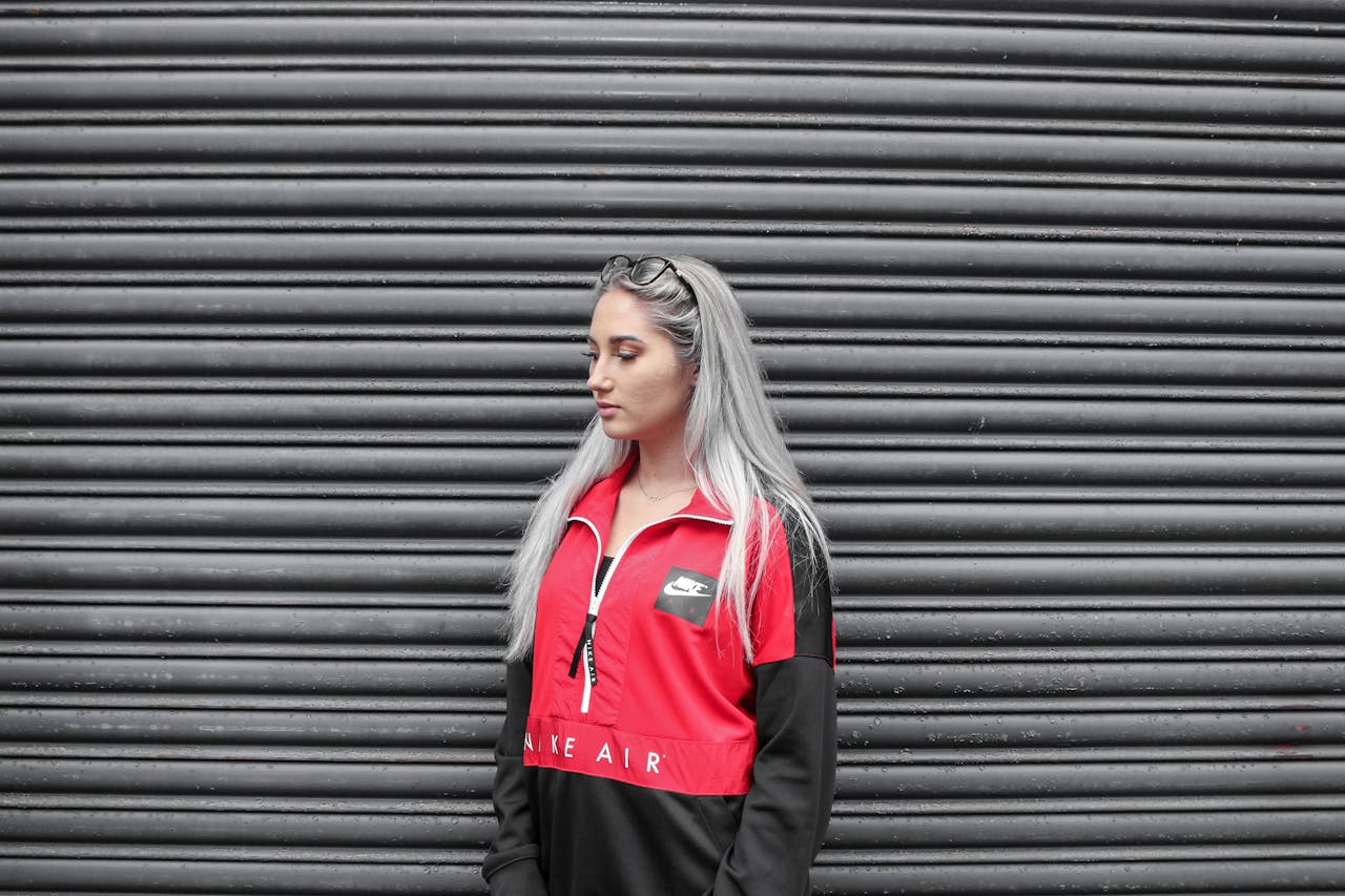 Fashionable woman in a red and black jacket poses against an urban metal wall.